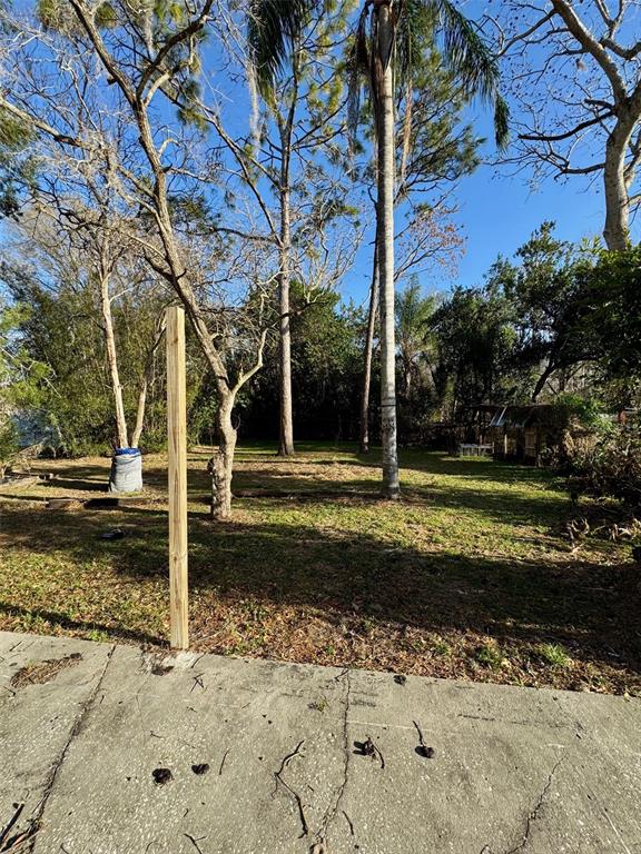 A wooden post stands on a concrete patio overlooking a grassy backyard with trees — 7700 VINE STREET, LAND O LAKES, FL