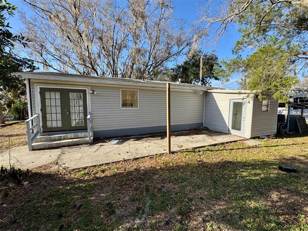 The exterior of a single-story house features light gray siding, a concrete patio, and trees — 7700 VINE STREET, LAND O LAKES, FL