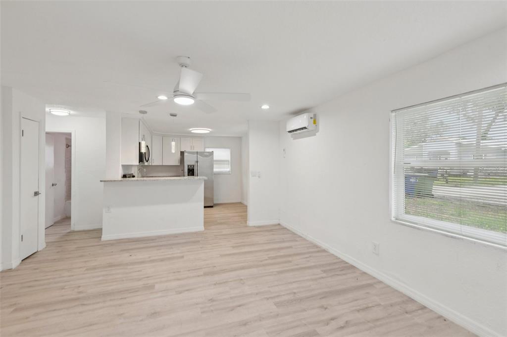 A bright room with light wood-look flooring, a white kitchen island, and a wall-mounted AC unit — 9404 N MULBERRY STREET, TAMPA, FL