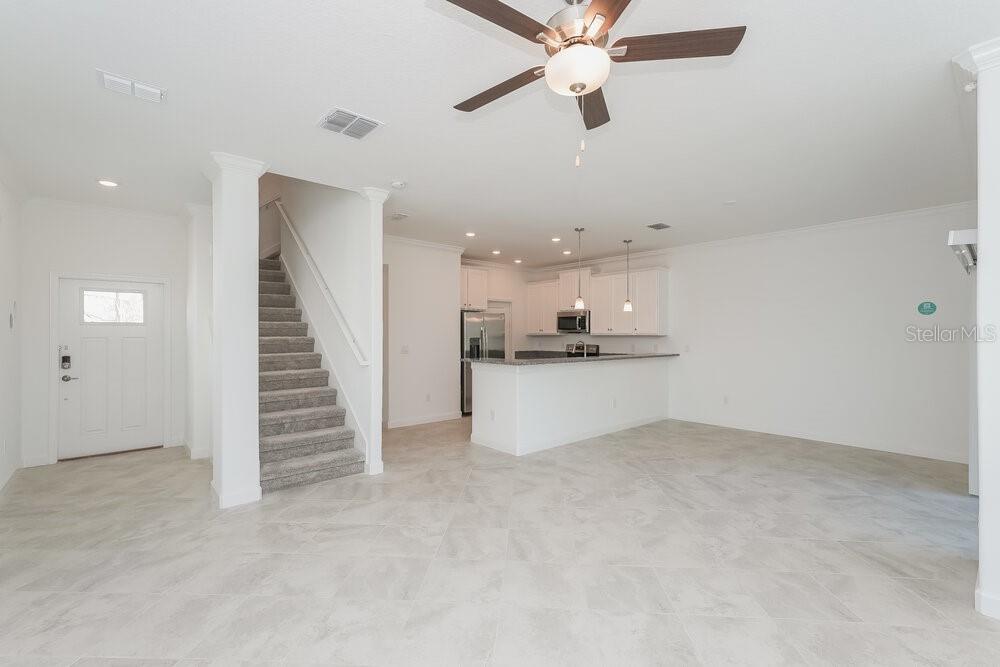 An open-concept living area features tile flooring, a carpeted staircase, and a kitchen with white cabinets — 17512 RADIANT SHINE WAY, LUTZ, FL
