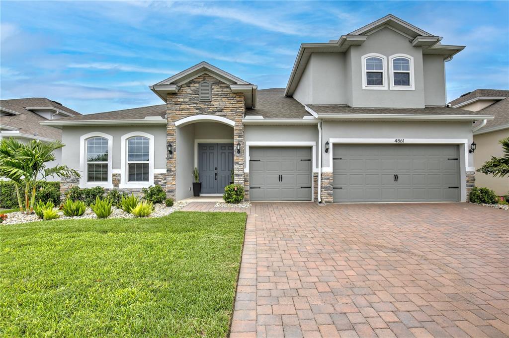 A two-story house with a stone-accented facade, gray garage doors, and a paved driveway — 4861 CRAGMERE LOOP, CLERMONT, FL