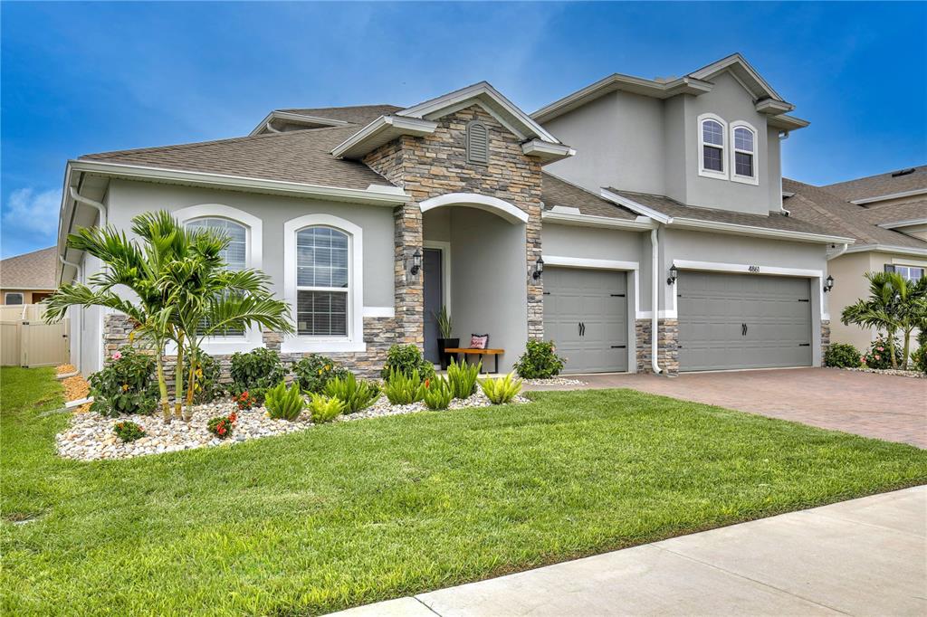 A two-story suburban house features a stone-accented facade, a gray garage, and a landscaped yard — 4861 CRAGMERE LOOP, CLERMONT, FL