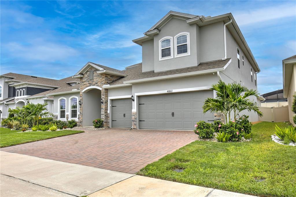 A two-story suburban house with a gray stucco exterior, stone accents, and a paved driveway — 4861 CRAGMERE LOOP, CLERMONT, FL