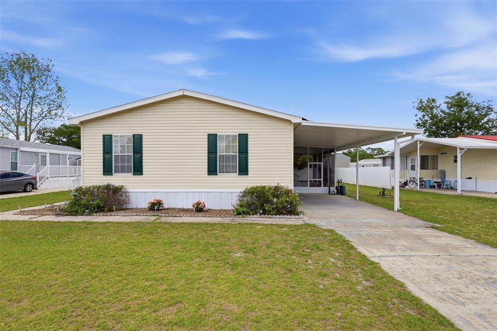A single-story manufactured home with light siding, green shutters, and an attached carport — 373 DOLORES BOULEVARD, DELAND, FL