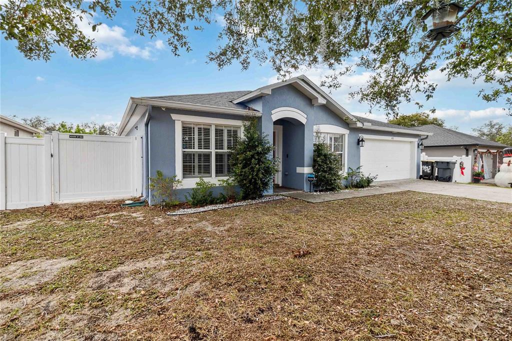 A blue single-story house with a white garage door, white fence, and a front yard — 402 RIO GRANDE COURT, POINCIANA, FL