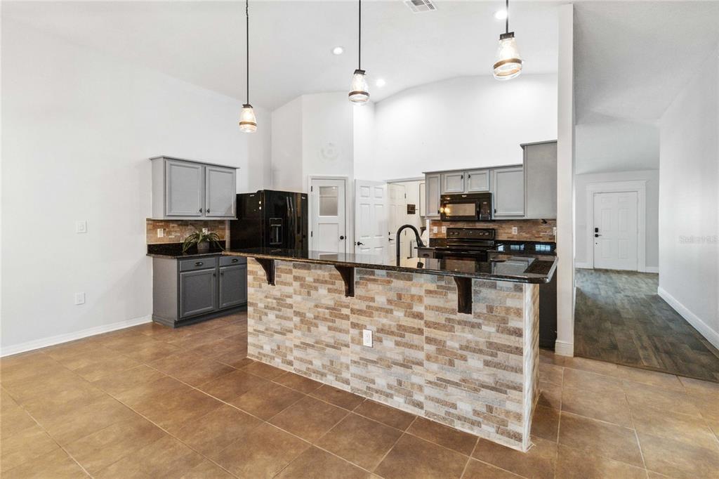 A kitchen features gray cabinets, black appliances, a stone-faced breakfast bar, and tile flooring — 402 RIO GRANDE COURT, POINCIANA, FL