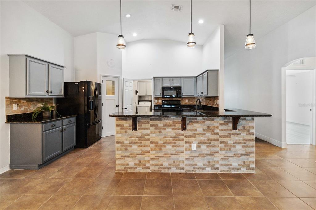 A kitchen features gray cabinets, black appliances, a stone-tiled island, and brown floor tiles — 402 RIO GRANDE COURT, POINCIANA, FL