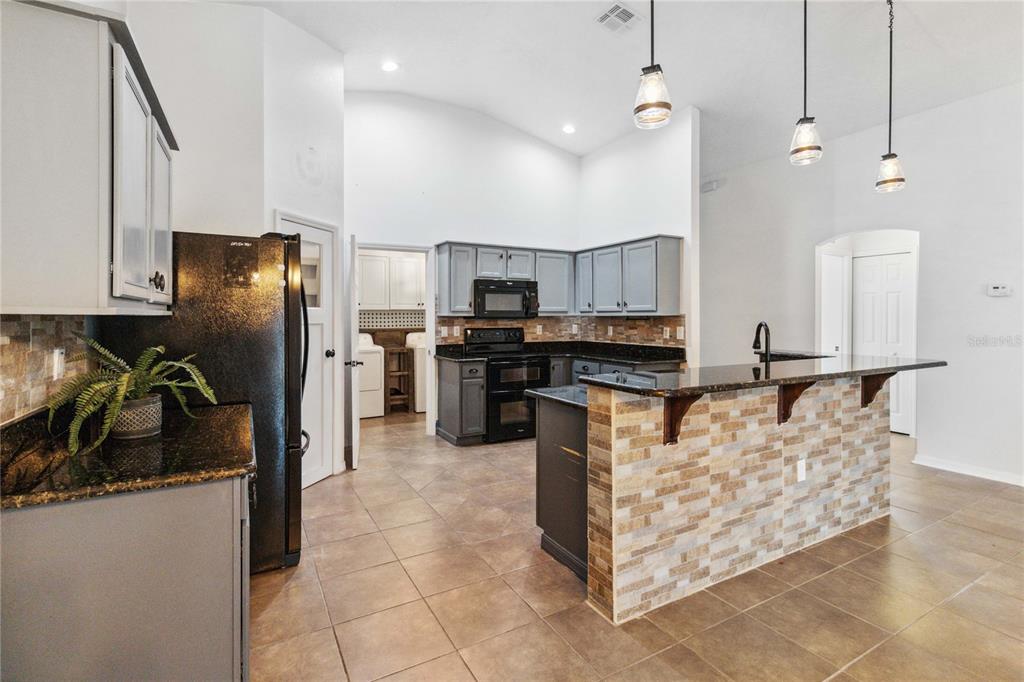 A kitchen features gray cabinets, dark granite countertops, a stone-tiled island, and tile flooring — 402 RIO GRANDE COURT, POINCIANA, FL