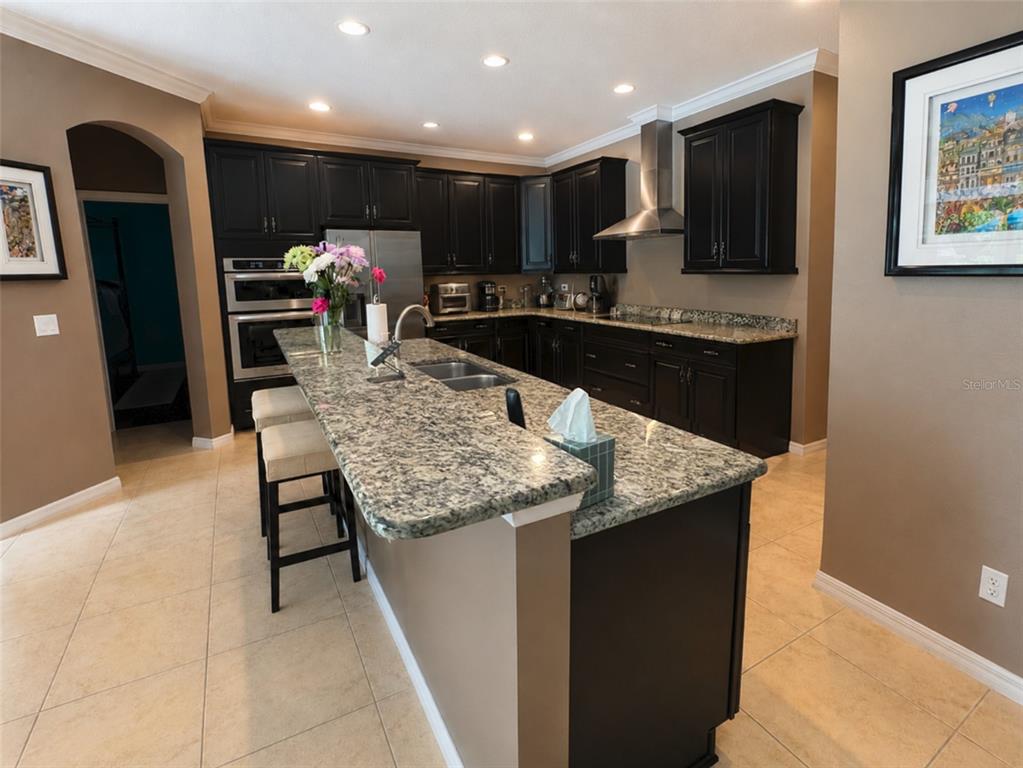 A kitchen features dark wood cabinets, granite countertops, a large island, and tile flooring — 1442 VIVALDI PLACE, LONGWOOD, FL