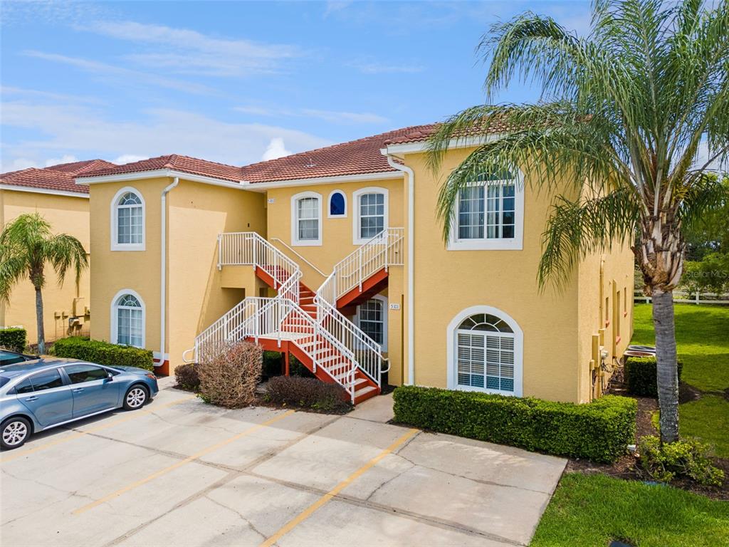 A two-story yellow stucco apartment building features an external staircase and a paved parking area — 5101 LAKE MARION GOLF RESORT UNIT 5101, KISSIMMEE, FL