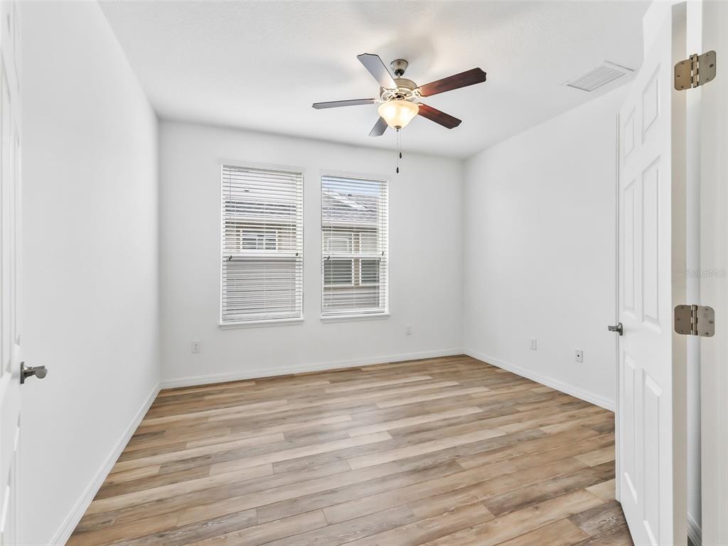 An empty bedroom features white walls, wood-look flooring, two windows with blinds, and a ceiling fan — 4976 NW 35TH LANE ROAD, OCALA, FL