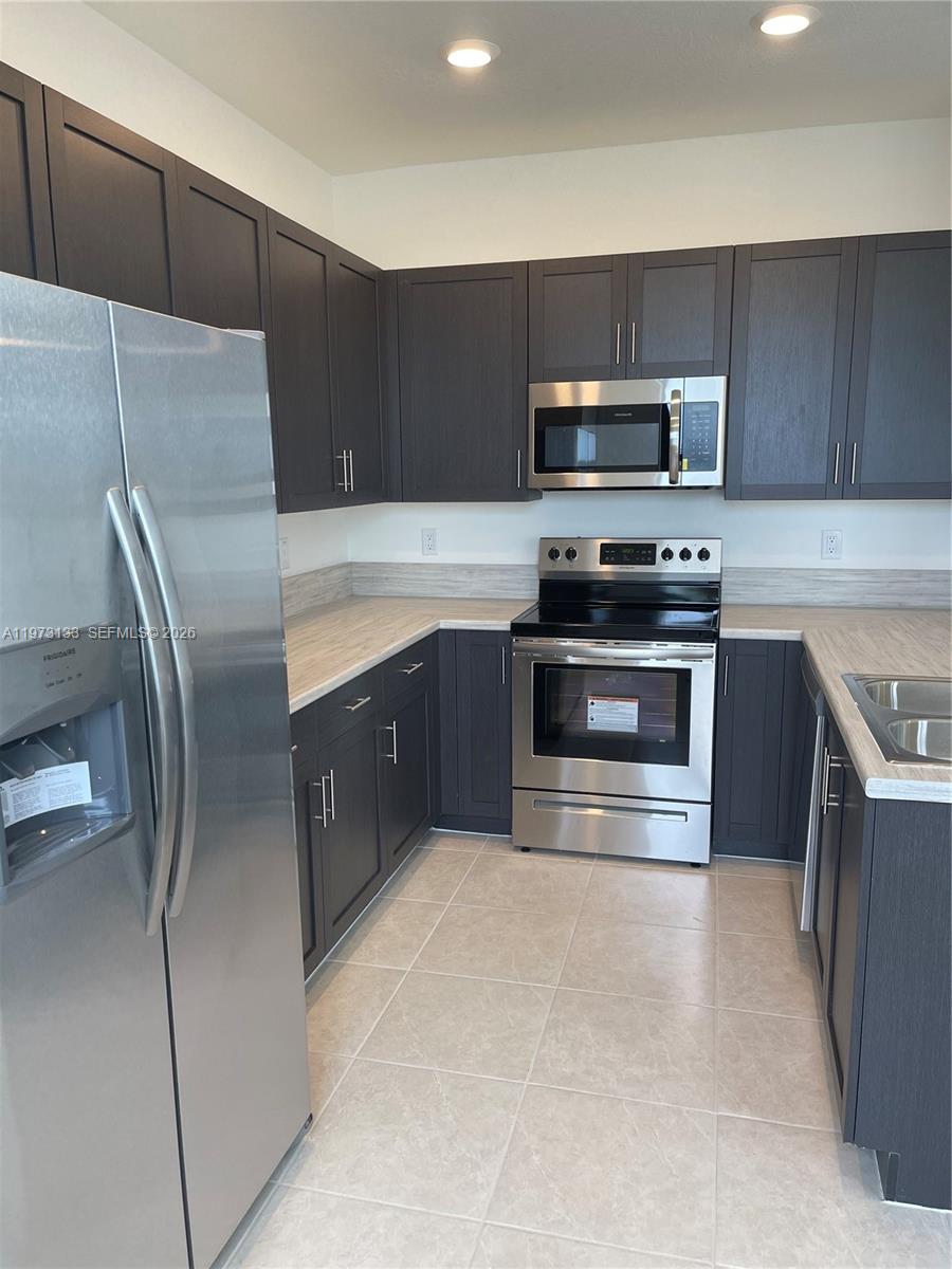A kitchen features dark wood cabinets, stainless steel appliances, and light-colored countertops — 20564 NE 5th Pl, Miami FL 33179, MIAMI, FL