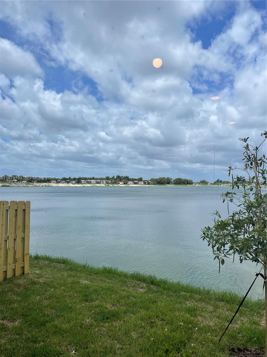 A view of a lake from a grassy yard with a wooden fence — 20564 NE 5th Pl, Miami FL 33179, MIAMI, FL
