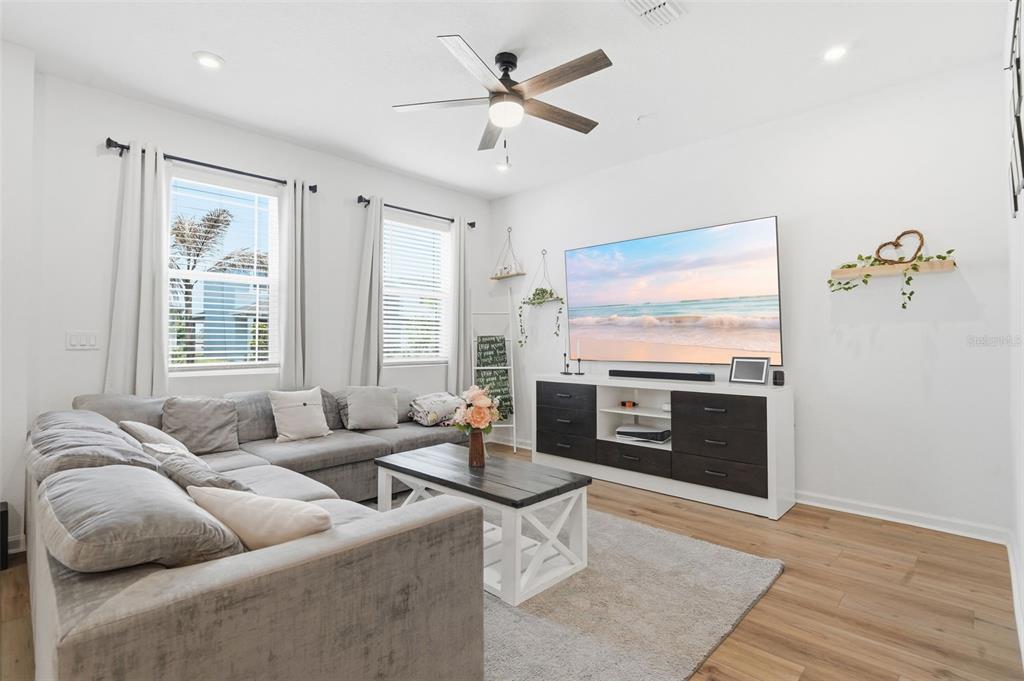 A living room features a gray sectional sofa, a television on a media console, and wood-look flooring — 11429 SUNSAIL AVENUE, ORLANDO, FL