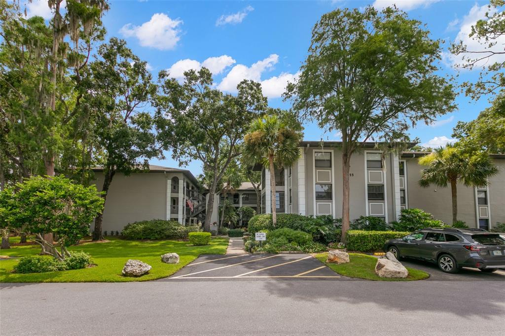 A multi-story apartment building with gray siding, surrounding trees, and a paved parking area — 3399 MERMOOR DRIVE UNIT 309, PALM HARBOR, FL