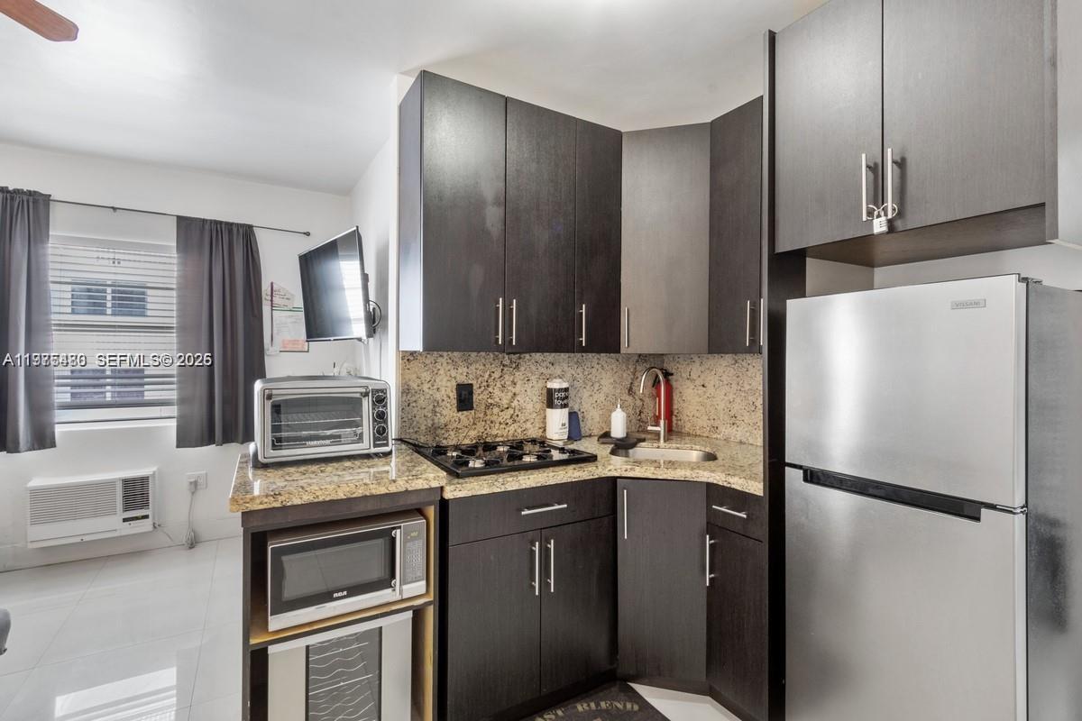 A compact kitchen features dark wood cabinets, granite countertops, stainless steel appliances, and a sink — 335 Ocean Dr # 310, Miami Beach FL 33139, MIAMI BEACH, FL