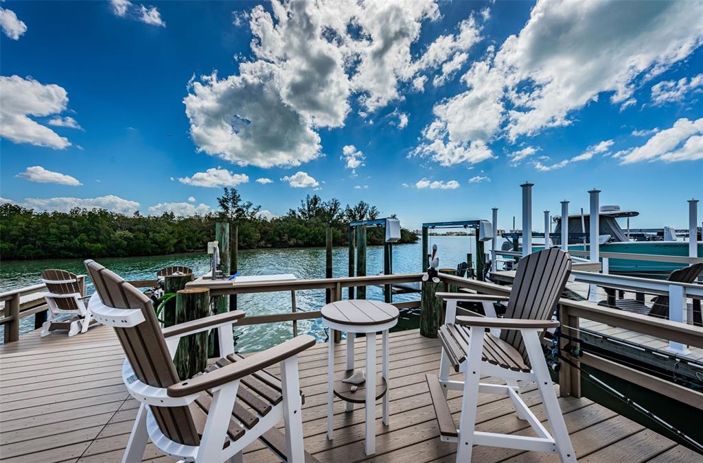A sunroom with tile flooring opens to a wooden deck overlooking a boat dock — 476 BOCA CIEGA POINT BOULEVARD S, ST PETERSBURG, FL