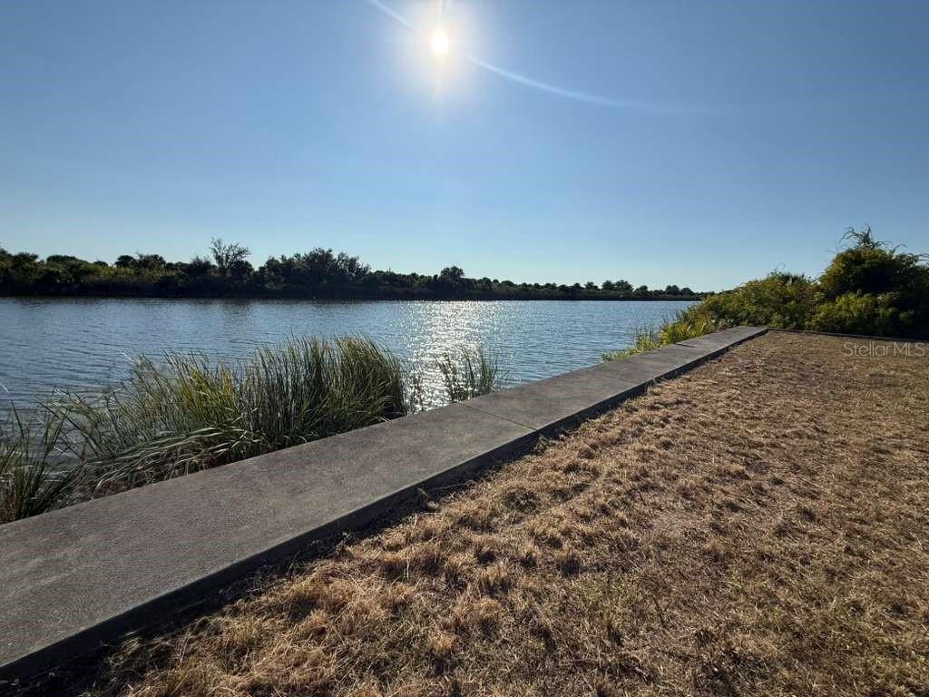 A concrete seawall borders a grassy yard overlooking a lake under a bright sun — 13421 GREENCASTLE AVENUE, PORT CHARLOTTE, FL