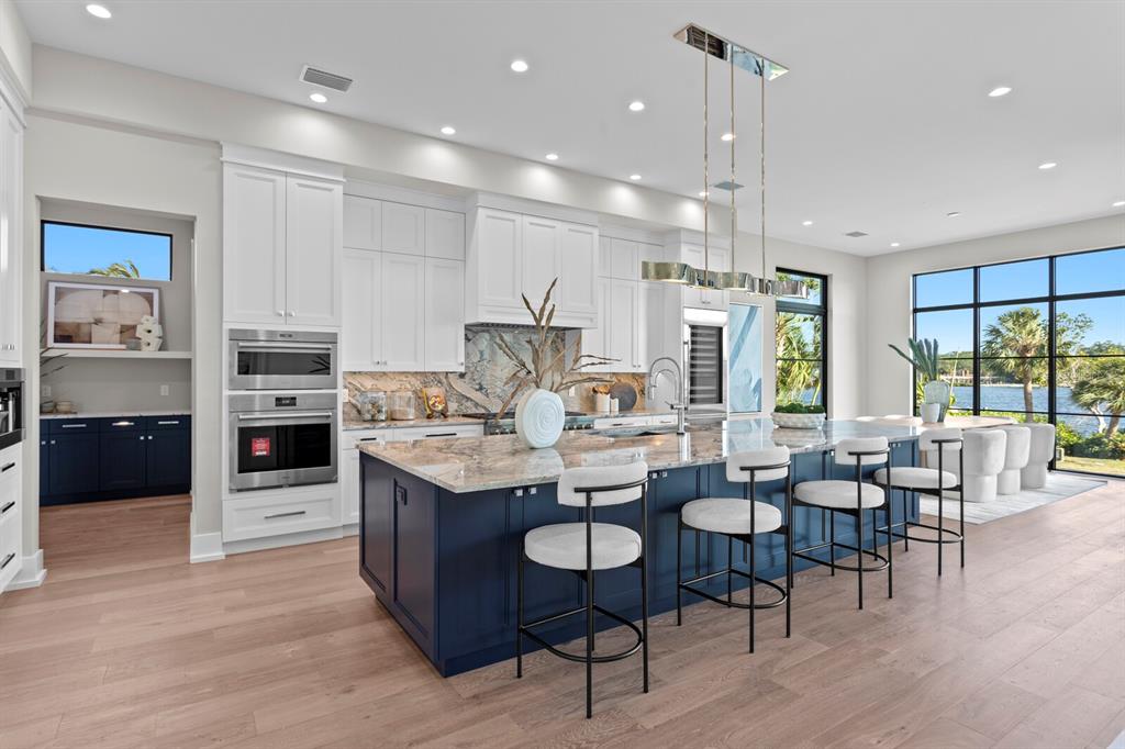 A modern kitchen features a large blue island, white cabinetry, and floor-to-ceiling windows overlooking water — 337 COFFEE POT DRIVE NE, ST PETERSBURG, FL