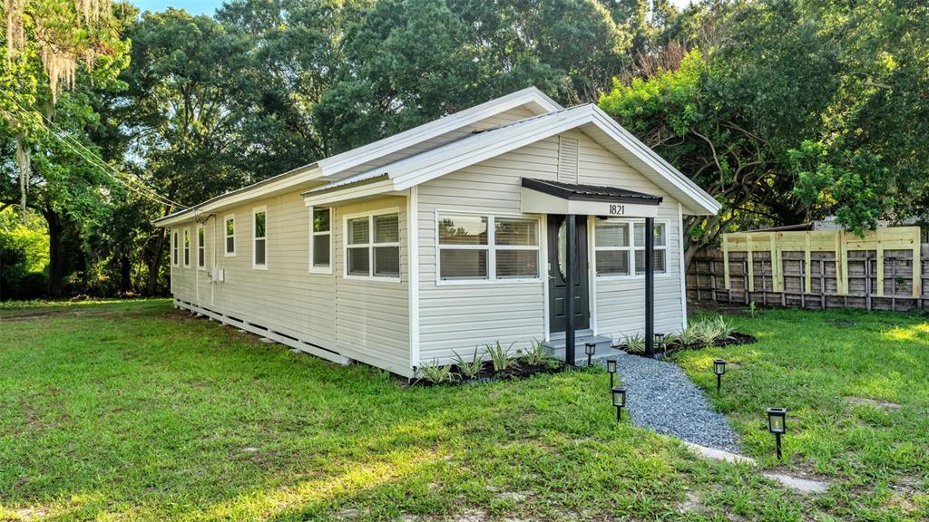 A single-story house with light-colored siding, a metal roof, and a gravel walkway — 1821 W CHASE STREET, LAKELAND, FL