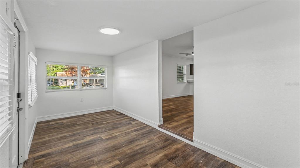 An empty room with wood-look flooring and white walls leads into an adjacent living area — 1821 W CHASE STREET, LAKELAND, FL