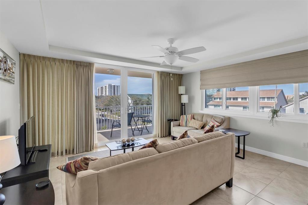 A living room with beige sofas, tile floors, a ceiling fan, and a balcony view — 223 ISLAND WAY UNIT 4A, CLEARWATER, FL
