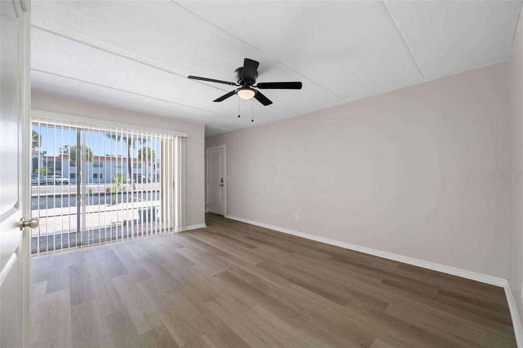 An empty room features wood-look flooring, a ceiling fan, and sliding glass doors to outside — 7950 BLIND PASS ROAD UNIT 4, ST PETERSBURG, FL