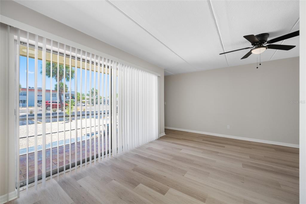 An empty room with light wood flooring, a ceiling fan, and vertical blinds over sliding doors — 7950 BLIND PASS ROAD UNIT 4, ST PETERSBURG, FL