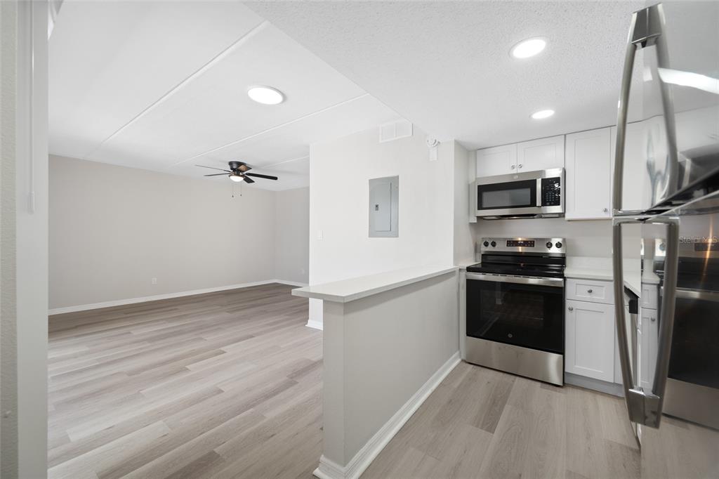A kitchen with stainless steel appliances and white cabinets overlooks an open living area — 7950 BLIND PASS ROAD UNIT 4, ST PETERSBURG, FL