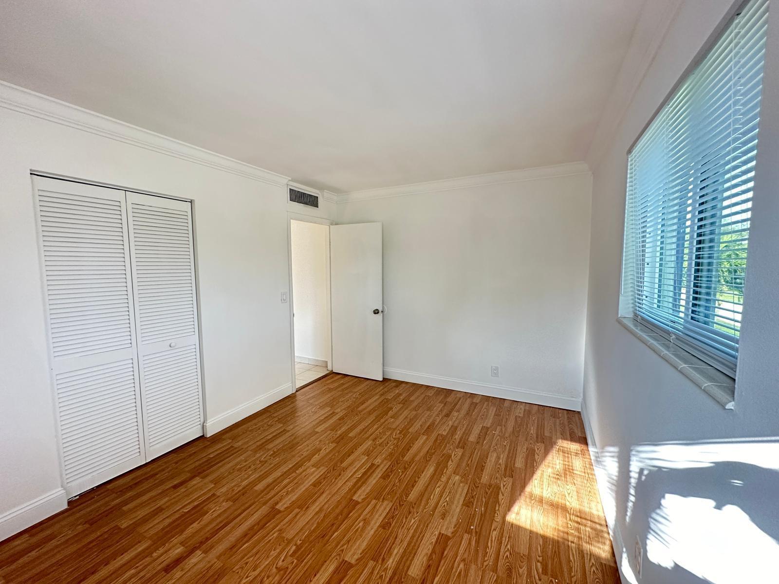 An empty bedroom with white walls, wood-look flooring, a louvered closet, and a window — 817 Lighthouse Drive # C, North Palm Beach FL 33408, NORTH PALM BEACH, FL