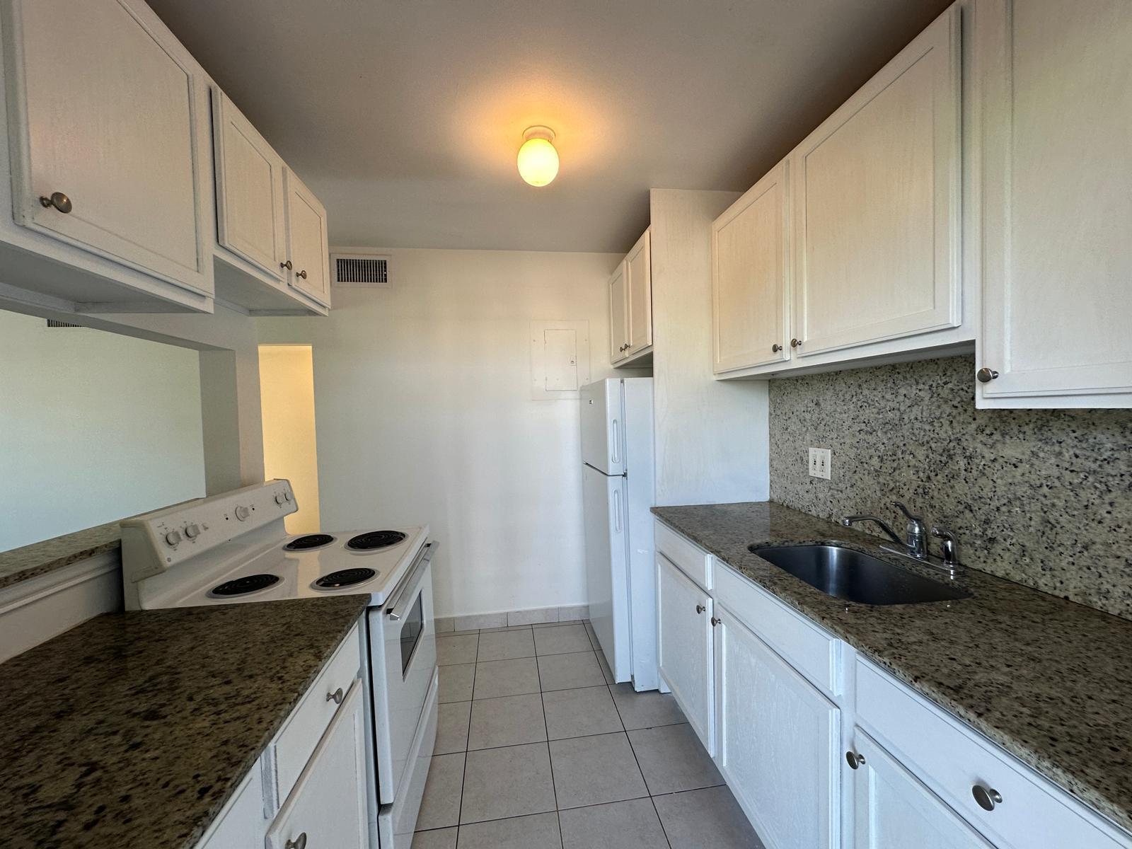 A kitchen features white cabinets, granite countertops, white appliances, and light-colored tile flooring — 817 Lighthouse Drive # C, North Palm Beach FL 33408, NORTH PALM BEACH, FL