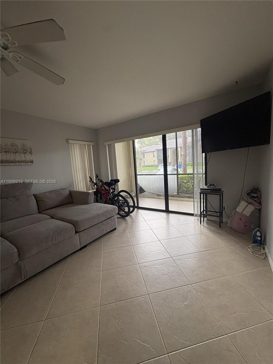 A living room features light tile flooring, a gray sectional sofa, and a sliding glass door — 718 Sunny Pine Way # D1, Green Acres FL 33415, GREEN ACRES, FL