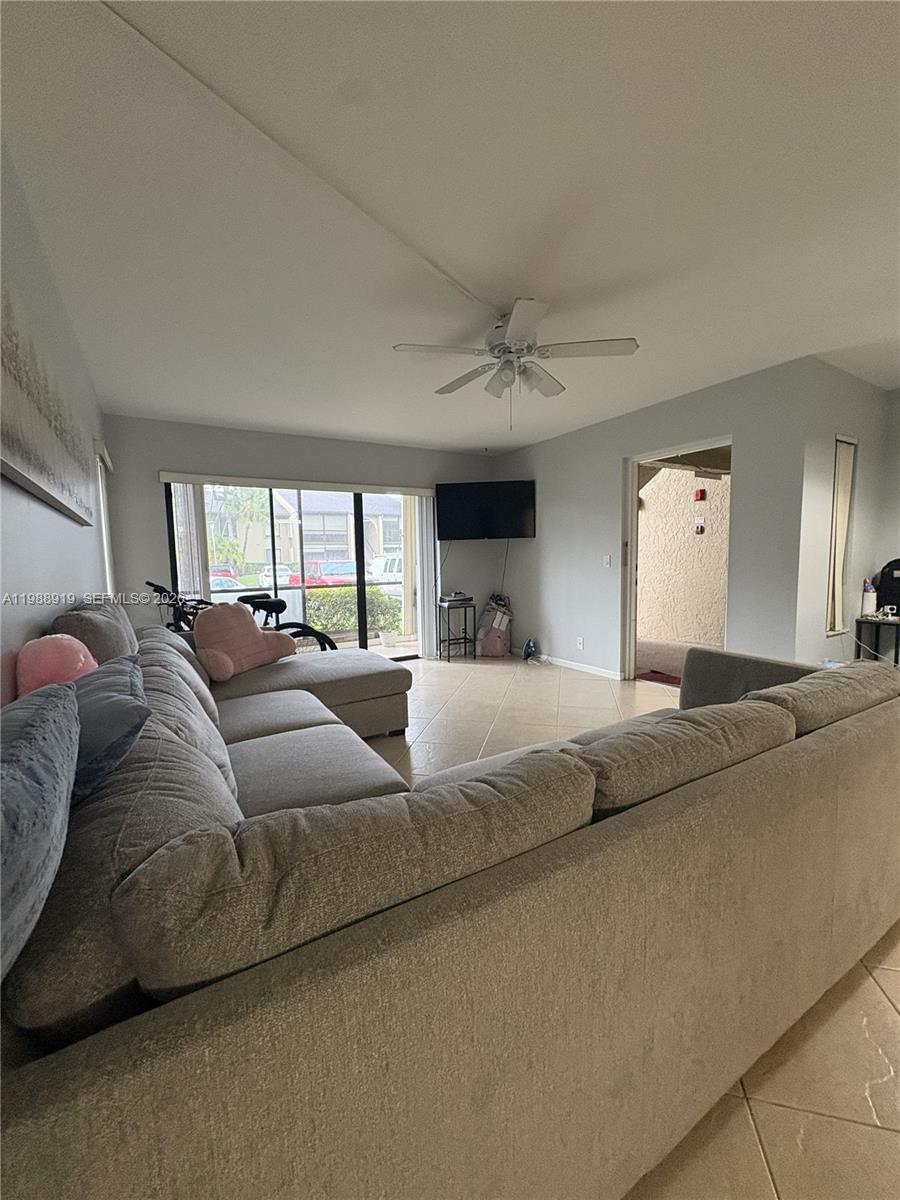 A living room features a large gray sectional sofa, tile flooring, and a ceiling fan — 718 Sunny Pine Way # D1, Green Acres FL 33415, GREEN ACRES, FL