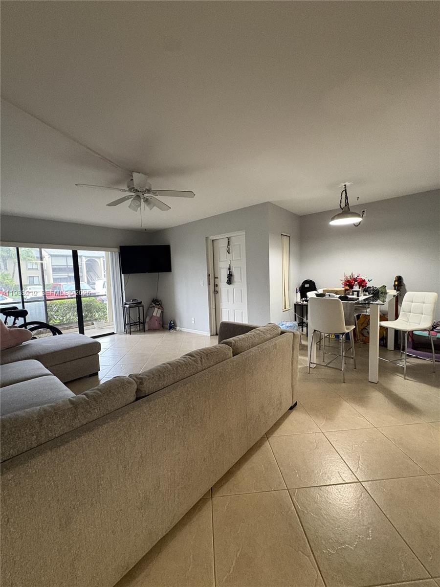A living room and dining area feature light tile flooring, a ceiling fan, and sliding doors — 718 Sunny Pine Way # D1, Green Acres FL 33415, GREEN ACRES, FL