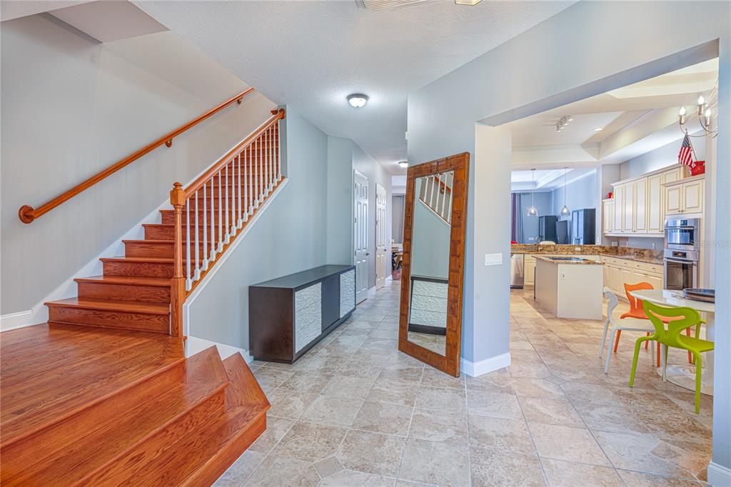 A foyer with a wooden staircase leads to an open kitchen with tile flooring — 3405 54TH DRIVE W UNIT 102, BRADENTON, FL