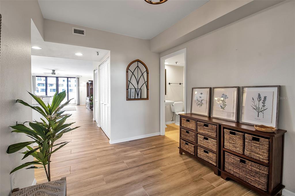A hallway with wood-look tile flooring, a potted plant, and a wooden storage unit — 1485 GULF OF MEXICO DRIVE UNIT 303, LONGBOAT KEY, FL