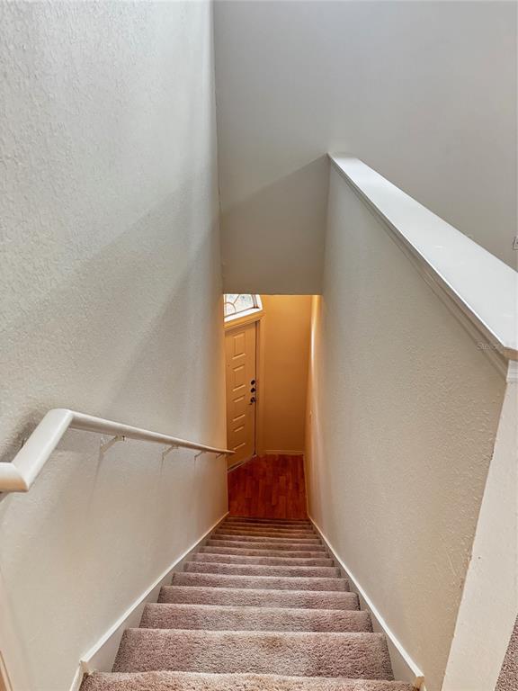 A carpeted staircase leads down to a landing with a wooden floor and front door — 1615 COLUMBIA ARMS CIRCLE UNIT 251, KISSIMMEE, FL