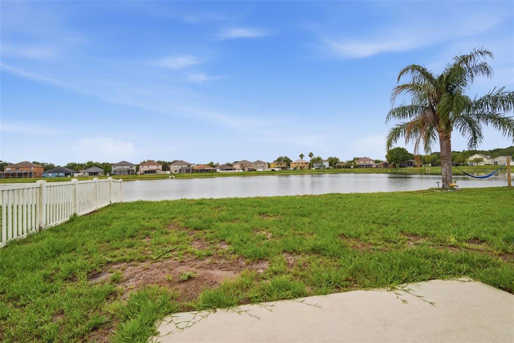 A grassy backyard features a white fence, a palm tree, and a view of a lake — 10604 LAKESIDE VISTA DRIVE, RIVERVIEW, FL