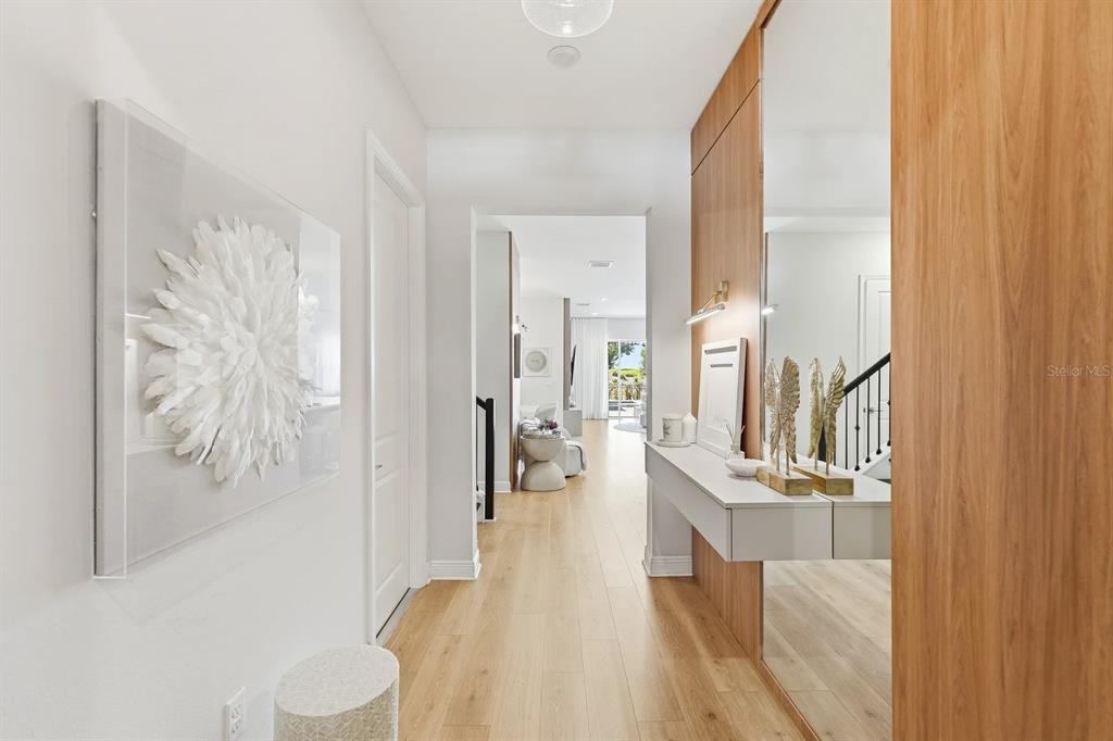 A modern hallway features light wood flooring, a floating console table, and a large mirror — 16312 VOLTERRA POINT, BELLA COLLINA, FL