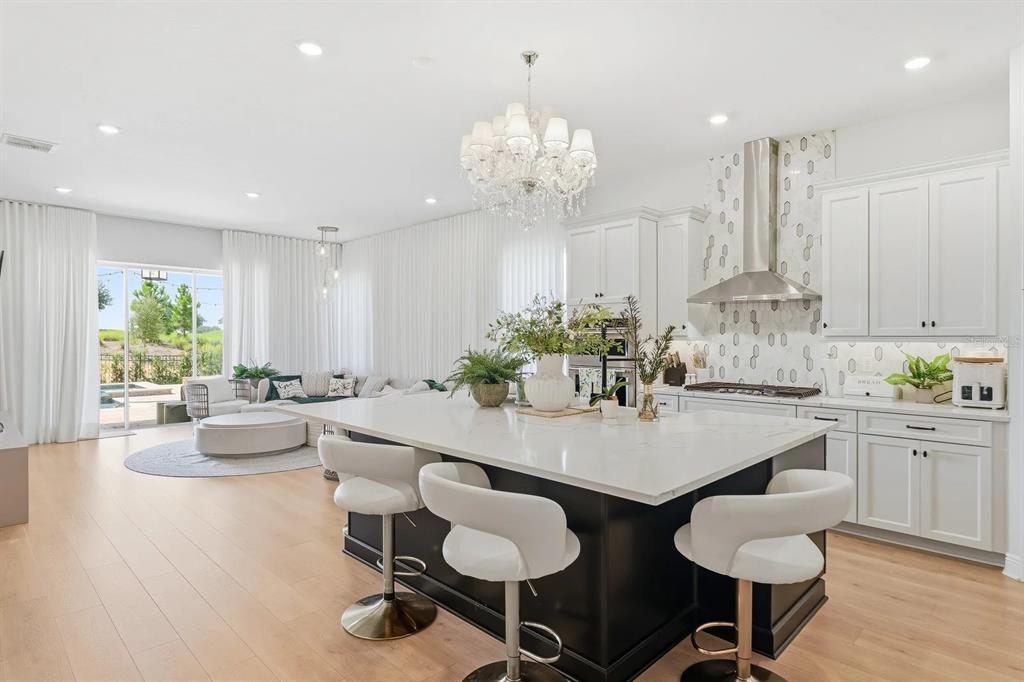 A modern kitchen features a large black island with white stools and white cabinetry — 16312 VOLTERRA POINT, BELLA COLLINA, FL