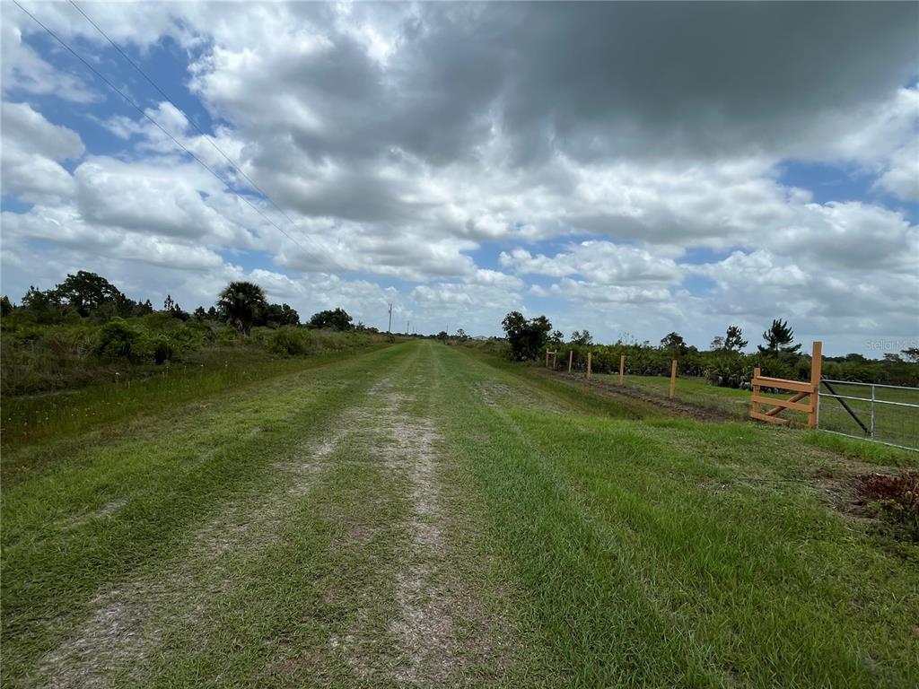 A grassy path leads through an open field bordered by a wooden fence and trees — 19092 NW 250TH STREET, OKEECHOBEE, FL
