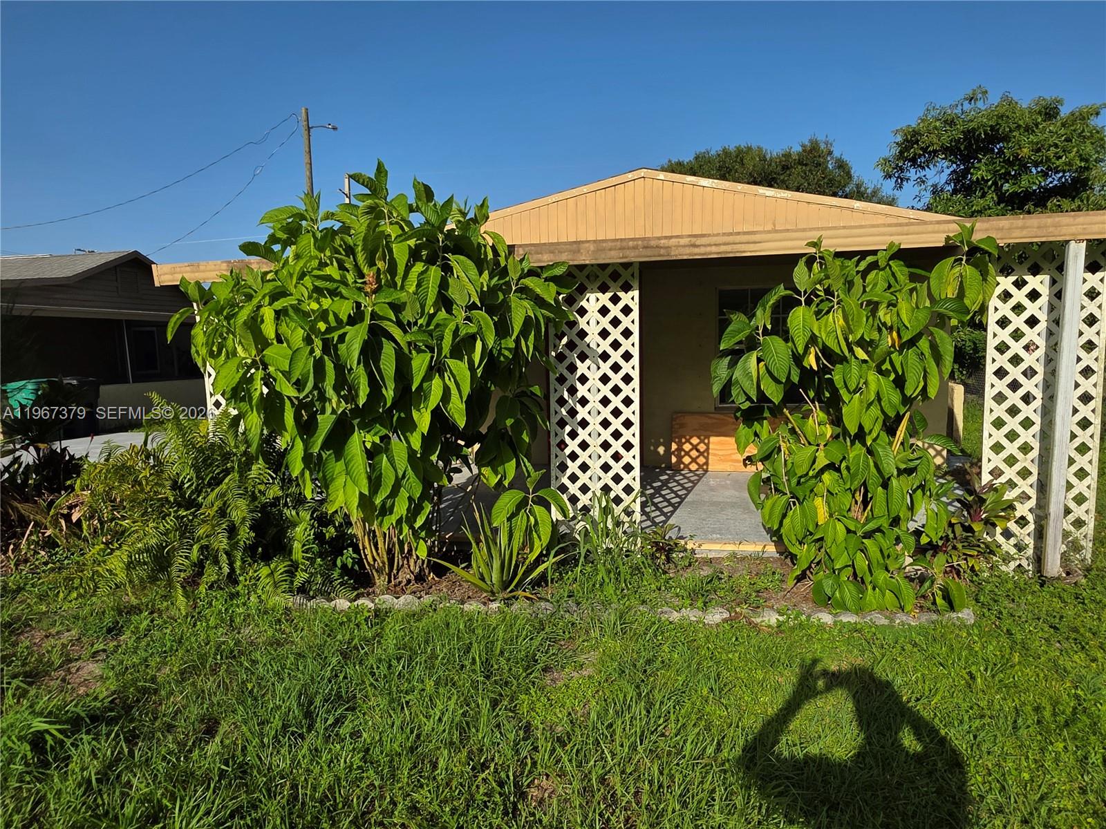 A small, tan house features a covered porch with white lattice screens and large shrubs — 4321 Kirby Loop Rd # 2, Fort Pierce FL 34981, FORT PIERCE, FL