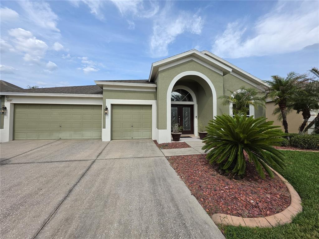 A single-story house with a three-car garage, arched entryway, and a landscaped front yard — 3608 JUNEBERRY DRIVE, WESLEY CHAPEL, FL