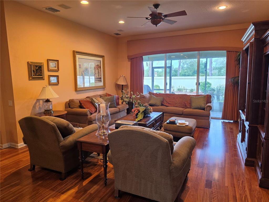 A living room features hardwood floors, a large sectional sofa, two armchairs, and sliding doors — 3608 JUNEBERRY DRIVE, WESLEY CHAPEL, FL