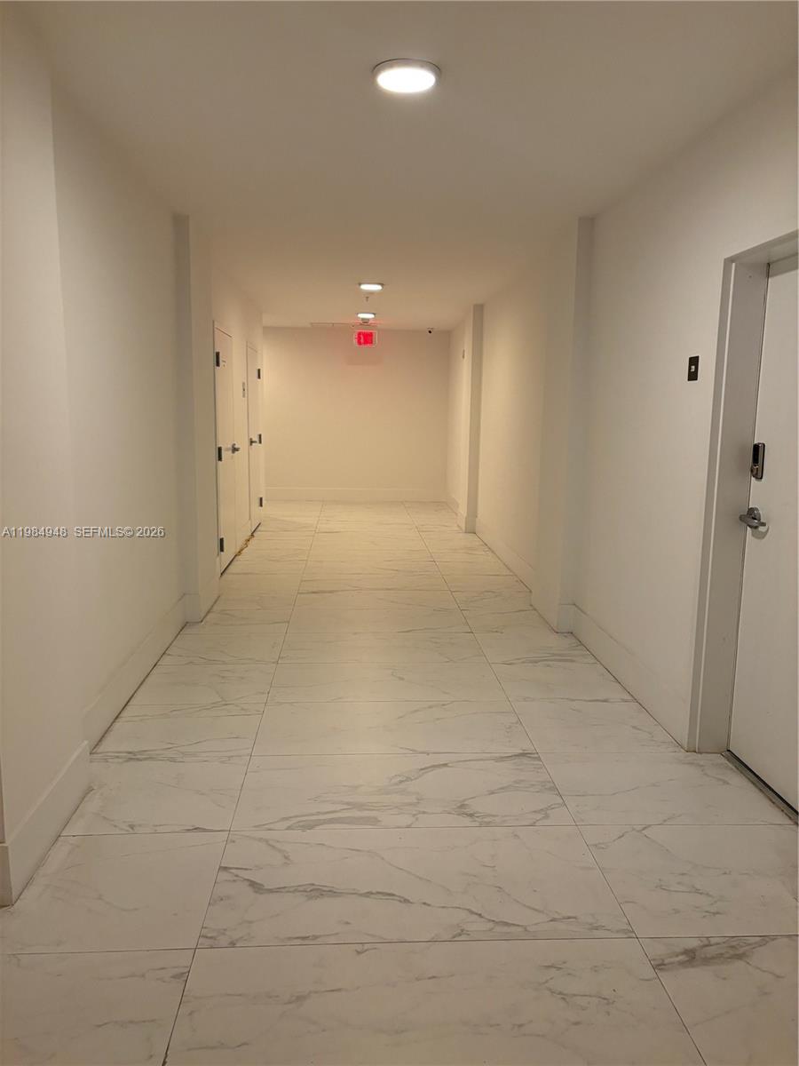 A long, narrow hallway features white marble-look tile flooring and white walls — 10950 NW 82nd St # 319, Doral FL 33178, DORAL, FL