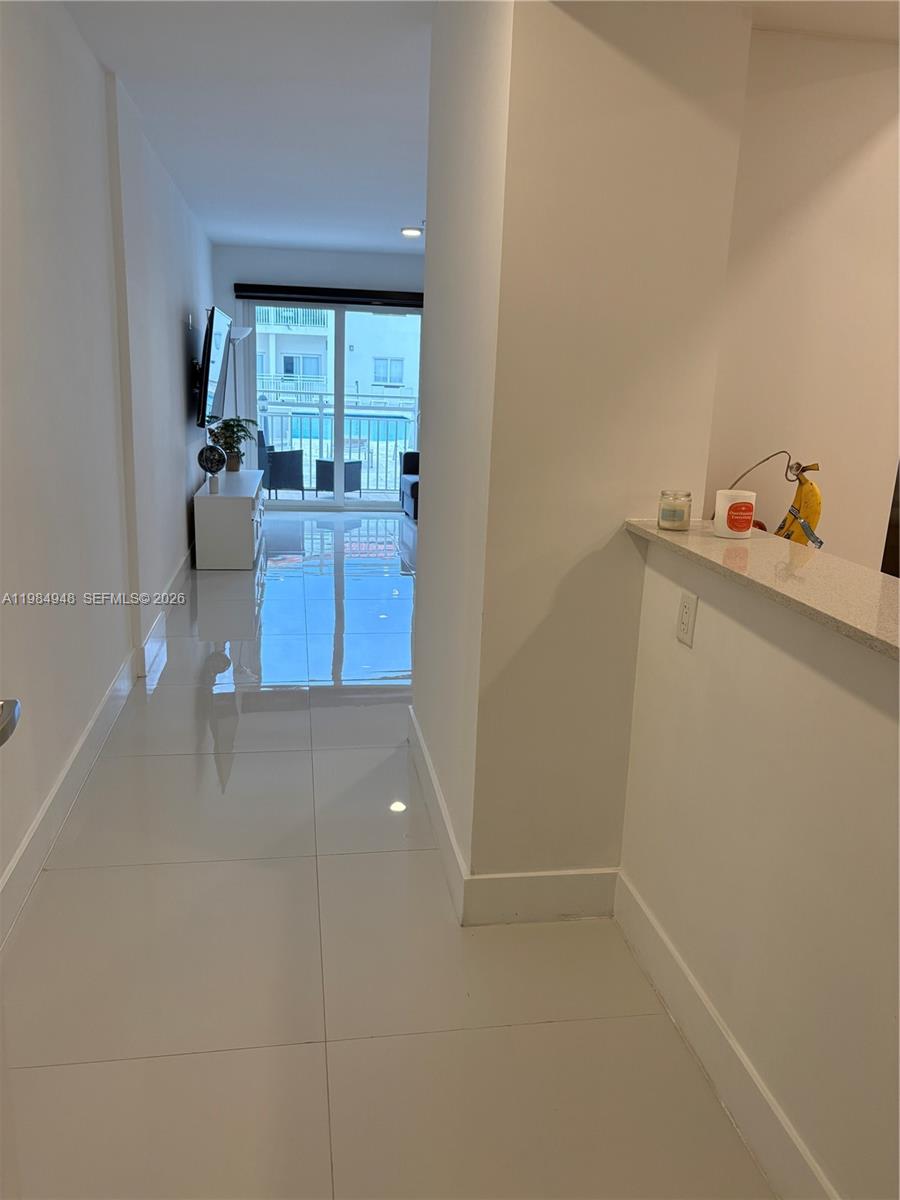 A hallway with white tile floors leads to a living area with a sliding glass door — 10950 NW 82nd St # 319, Doral FL 33178, DORAL, FL