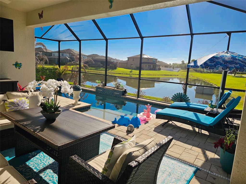 A covered patio features a pool, lounge chairs, and a dining set overlooking a lake — 12860 SATIN LILY DRIVE, RIVERVIEW, FL