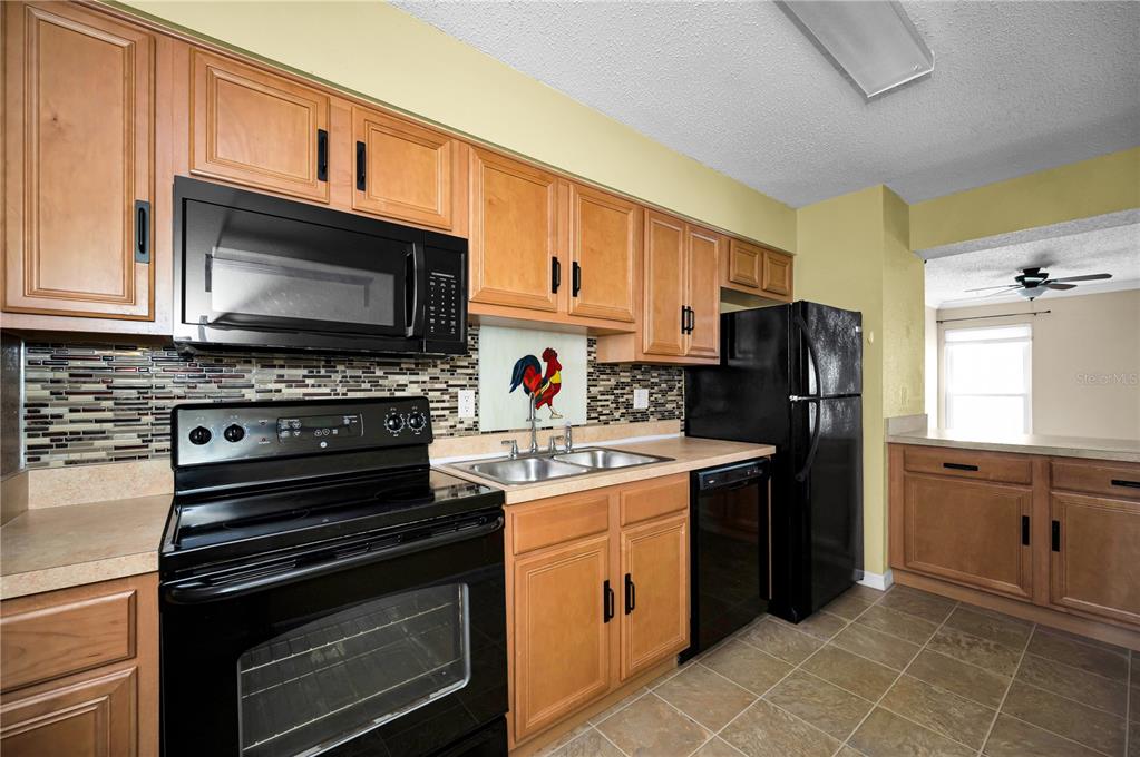 A kitchen features light wood cabinets, black appliances, a tiled backsplash, and tile flooring — 743 HAVEN PLACE UNIT 743, TARPON SPRINGS, FL