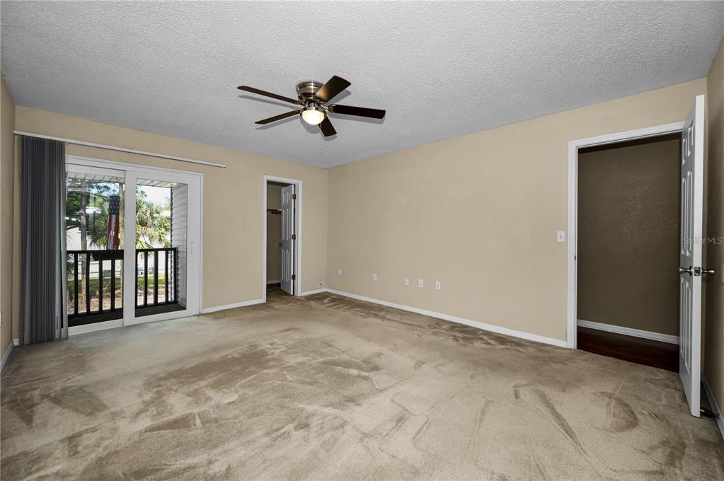 An empty bedroom features beige carpet, a ceiling fan, a sliding glass door, and two doorways — 743 HAVEN PLACE UNIT 743, TARPON SPRINGS, FL