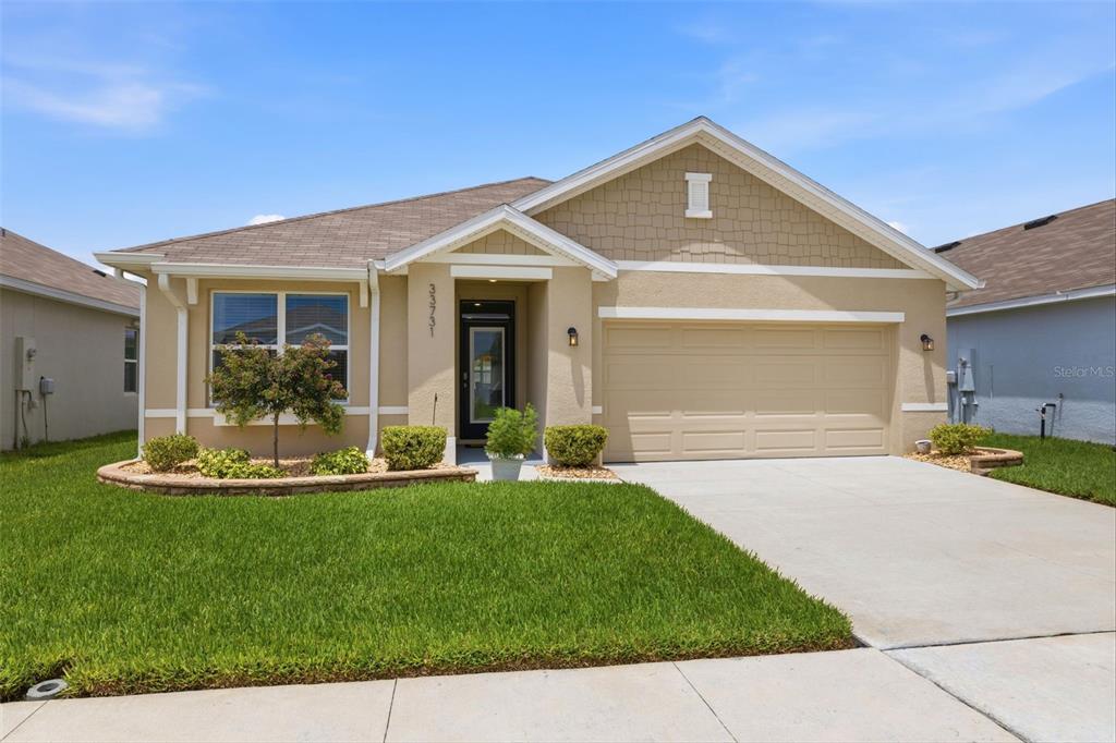 A single-story house with a tan stucco exterior, a two-car garage, and a front lawn — 33731 HAMILTON HILL LANE, WESLEY CHAPEL, FL